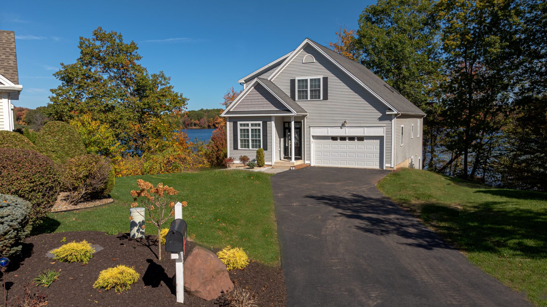 Lakefront home in Berlin, Connecticut with well-maintained landscaping and fall foliage in the background, showing a clean driveway and seasonal yard care.