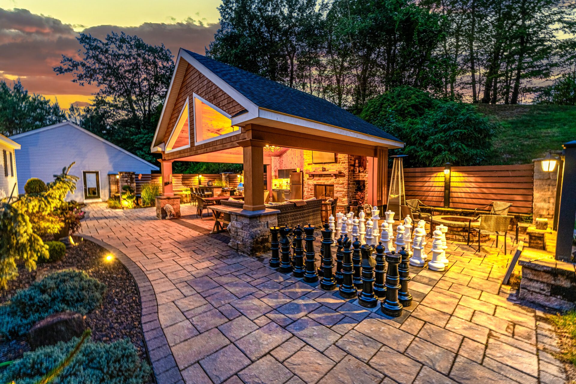 Outdoor covered patio with stone pavers, fire feature, and evening lighting in Berlin, Connecticut, showing a completed fall hardscaping project.